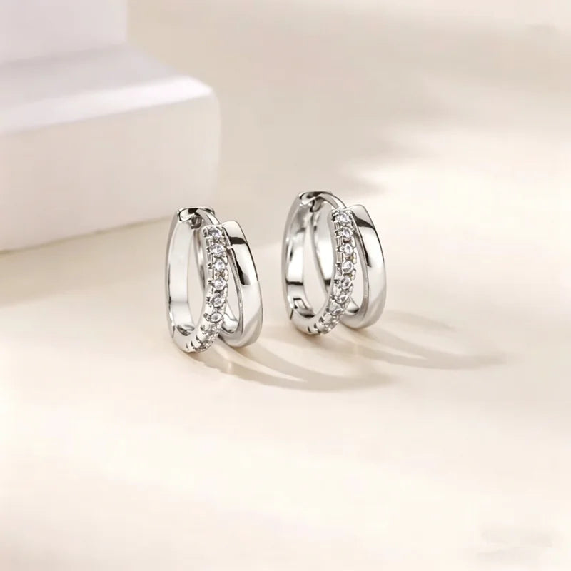 Pendientes de aro plateados con piedras de circonita cúbica, mostrados sobre una superficie blanca.