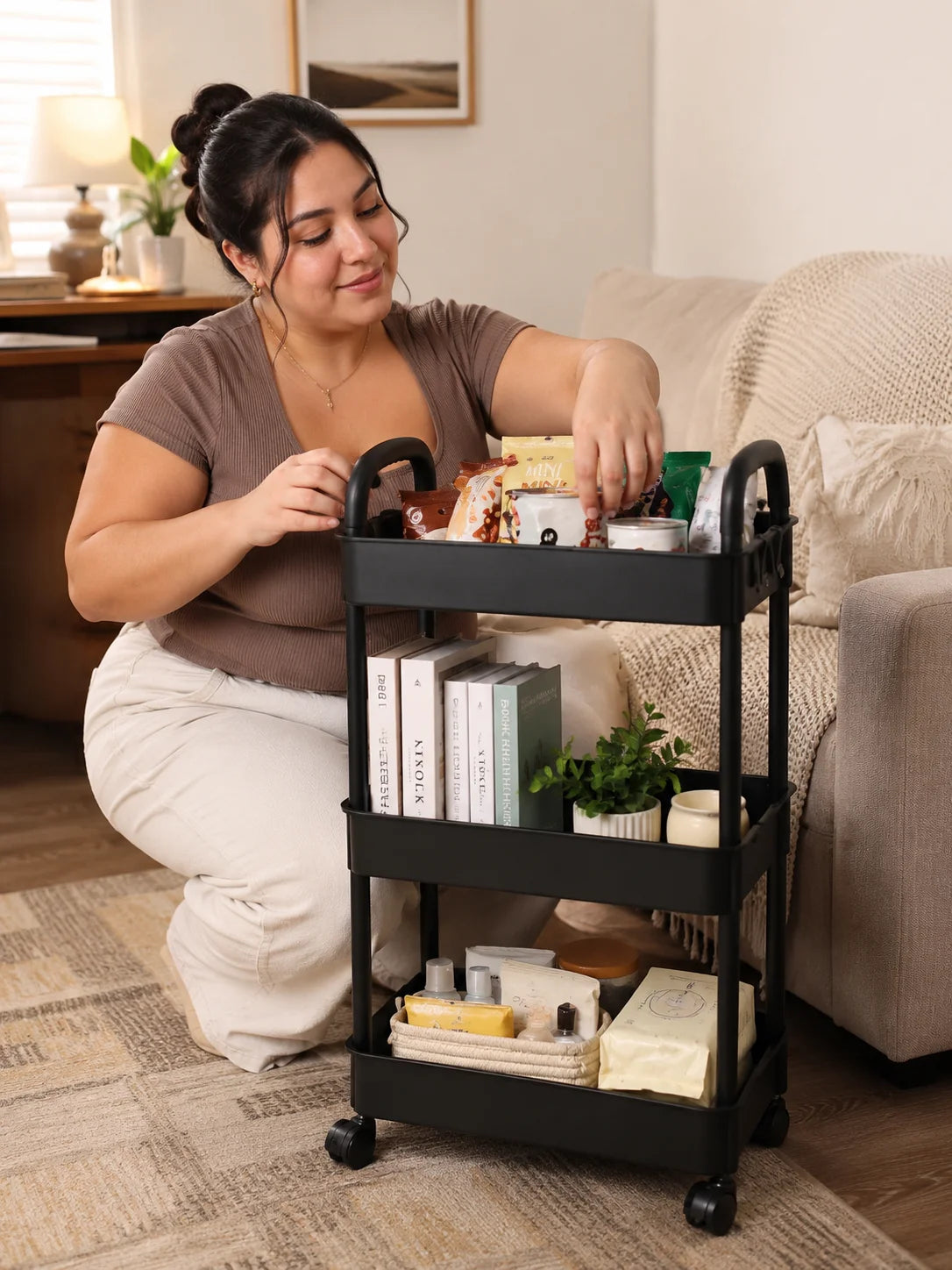 A woman is using a black 3-tier rolling utility cart to organize various items on a wooden floor.