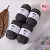 A skein of dark gray Milk Cotton yarn is shown next to a dried leaf, ready for knitting or crochet.
