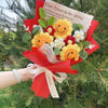 Ein Strauß handgefertigter Häkelblumen in Gelb-, Rot- und Weißtönen, in rohem Papier eingewickelt.