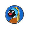 An enamel pin featuring a cartoon penguin with black skin, blue head covering, and an orange body.