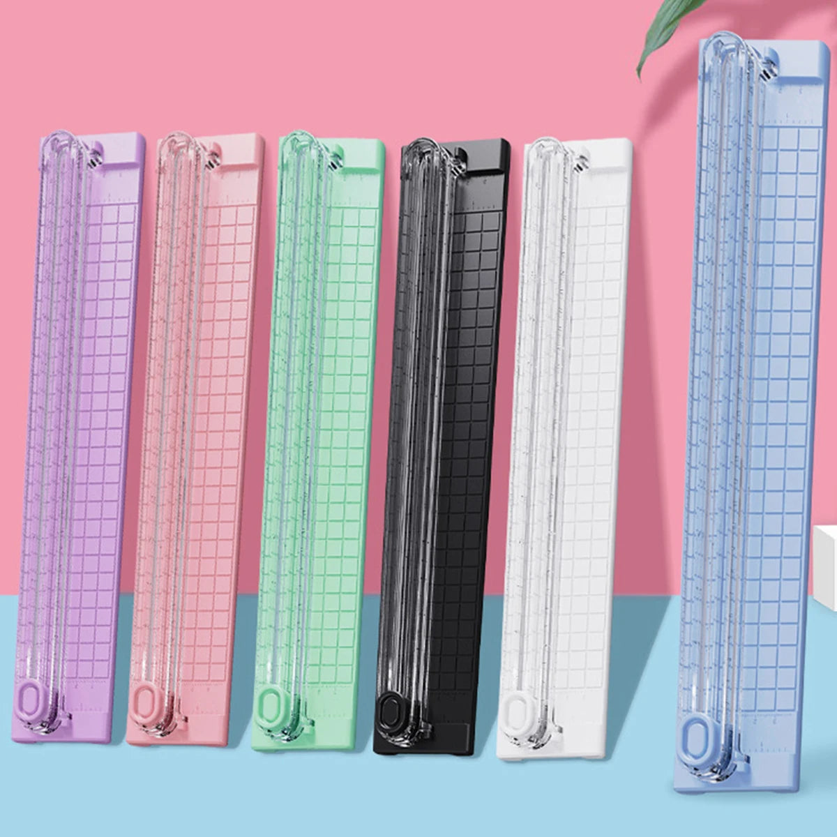 A row of colorful portable paper cutters or trimmers in various shades including purple, pink, green, black, and white.