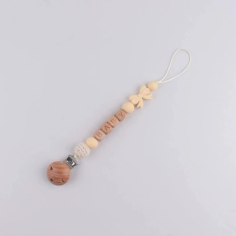 A beaded silicone pacifier clip lanyard with a name charm and a wooden teething sphere.