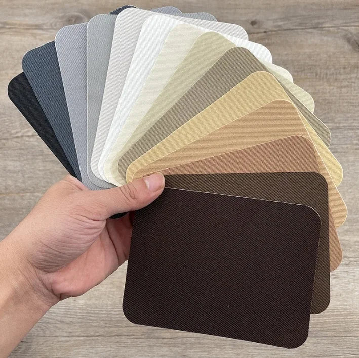 A hand holds a stack of iron-on fabric patches in various shades of gray, beige, and brown.