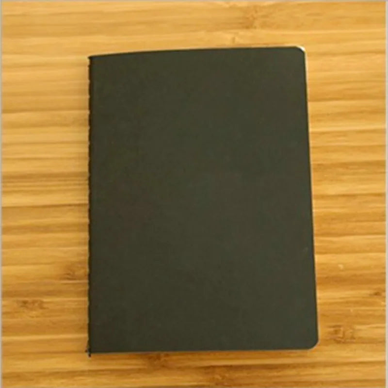 A black A6 Kraft paper blank notebook for sketching and journaling placed on a wooden surface.