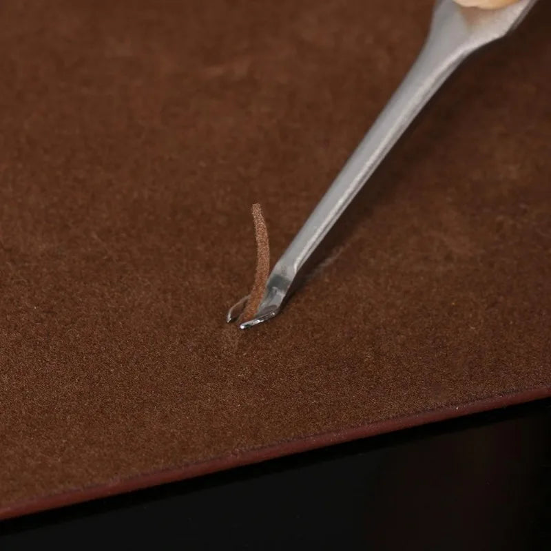 A silver tool is shown applying a groove to a piece of brown leather.