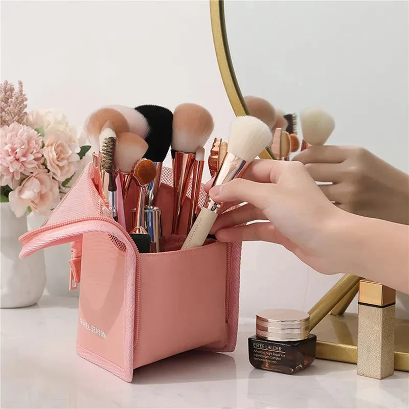 A pink waterproof makeup brush holder with a foldable stand and several makeup brushes is shown on a white surface.
