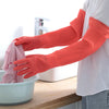 A person wearing bright orange silicone scrubbing gloves is washing a pink item in a white bowl.