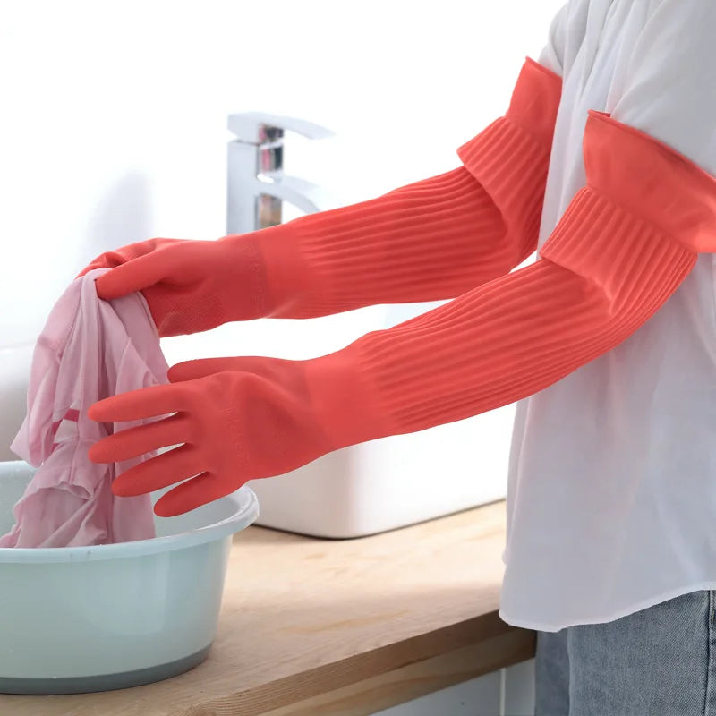 A person wearing bright orange silicone scrubbing gloves is washing a pink item in a white bowl.