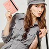 A woman wearing a gray uniform shirt holds a pink passport wallet and sunglasses.