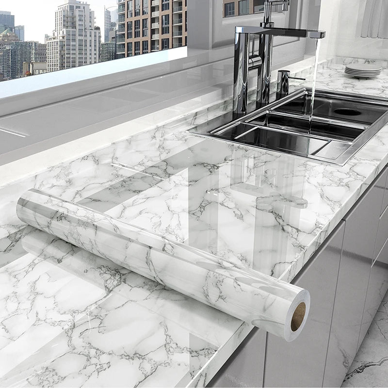 A stainless steel kitchen sink and faucet installed in a white marble countertop with a long marble effect film rolled out.