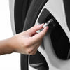 A hand is inserting a metal valve cap into an aluminum alloy wheel tire valve stem.