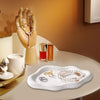 A white cloud-shaped jewelry tray holds gold and pearl jewelry next to a hand model.