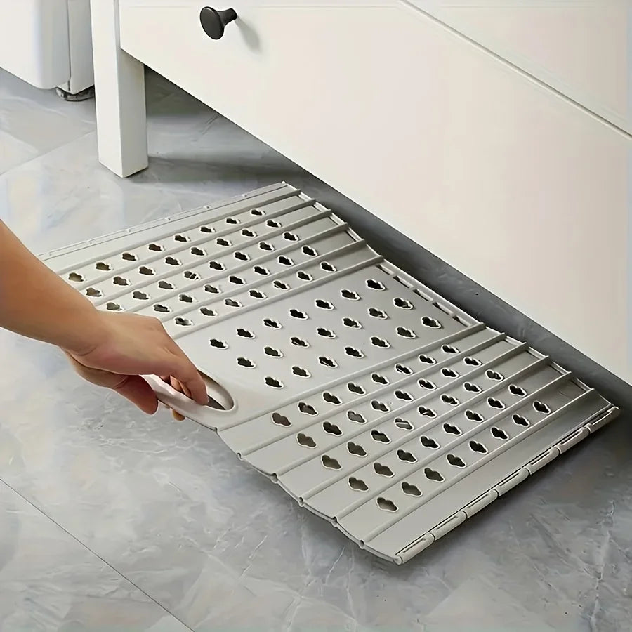 A hand is holding a folding laundry basket with handles, positioned next to a white cabinet.