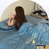 A person is lying in a blue comforter with embroidery, suggesting a cool experience for sleep.