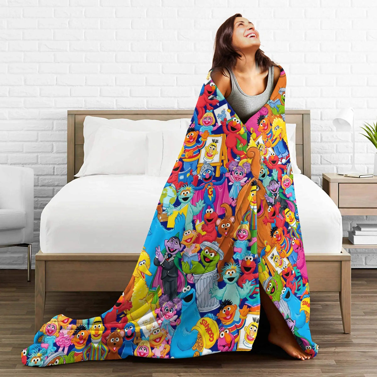 A woman is lying on a bed with a colorful Sesame Street Friends flannel throw blanket draped over her.