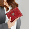 A close-up of a red leather wallet with stitching and a decorative metal accent, held by a person.