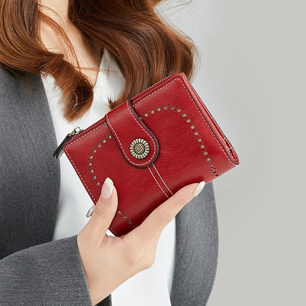 A close-up of a red leather wallet with stitching and a decorative metal accent, held by a person.