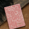 A pink leopard print passport holder with gold embossed personalization resting on a brown surface.