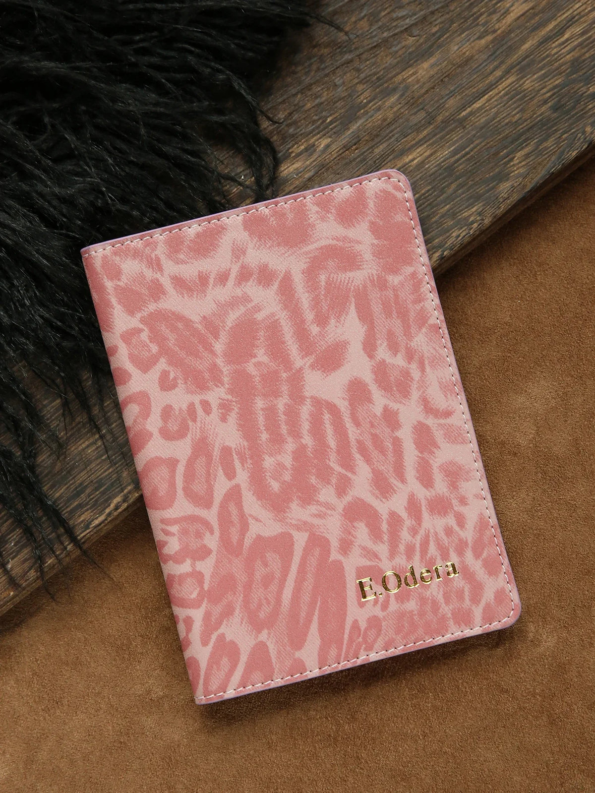 A pink leopard print passport holder with gold embossed personalization resting on a brown surface.
