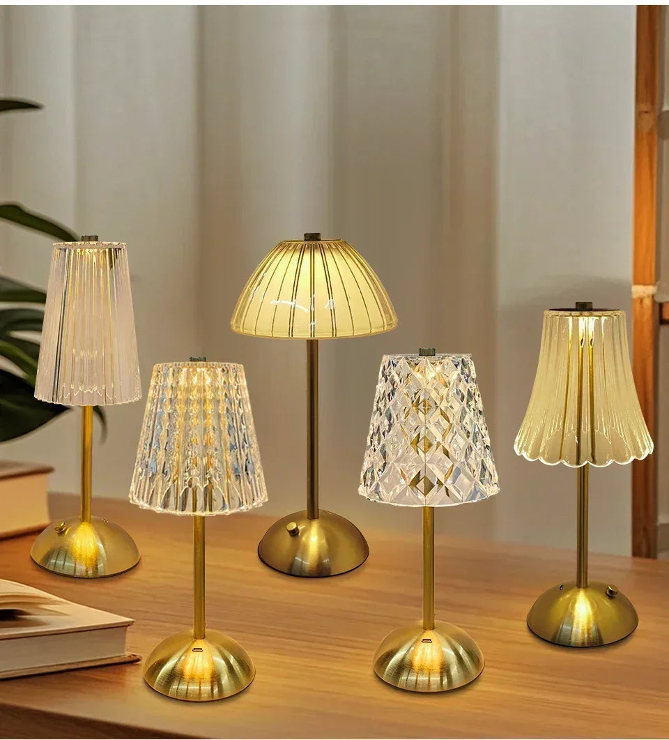 A collection of four gold-toned crystal touch table lamps with amber glass shades displayed on a wooden surface.