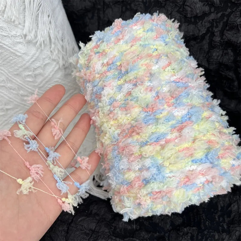A hand is holding a fluffy, variegated yarn blend featuring pastel pink, blue, and yellow fibers.