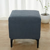 A dark blue geometric jacquard stretch ottoman cover placed on a wooden floor.