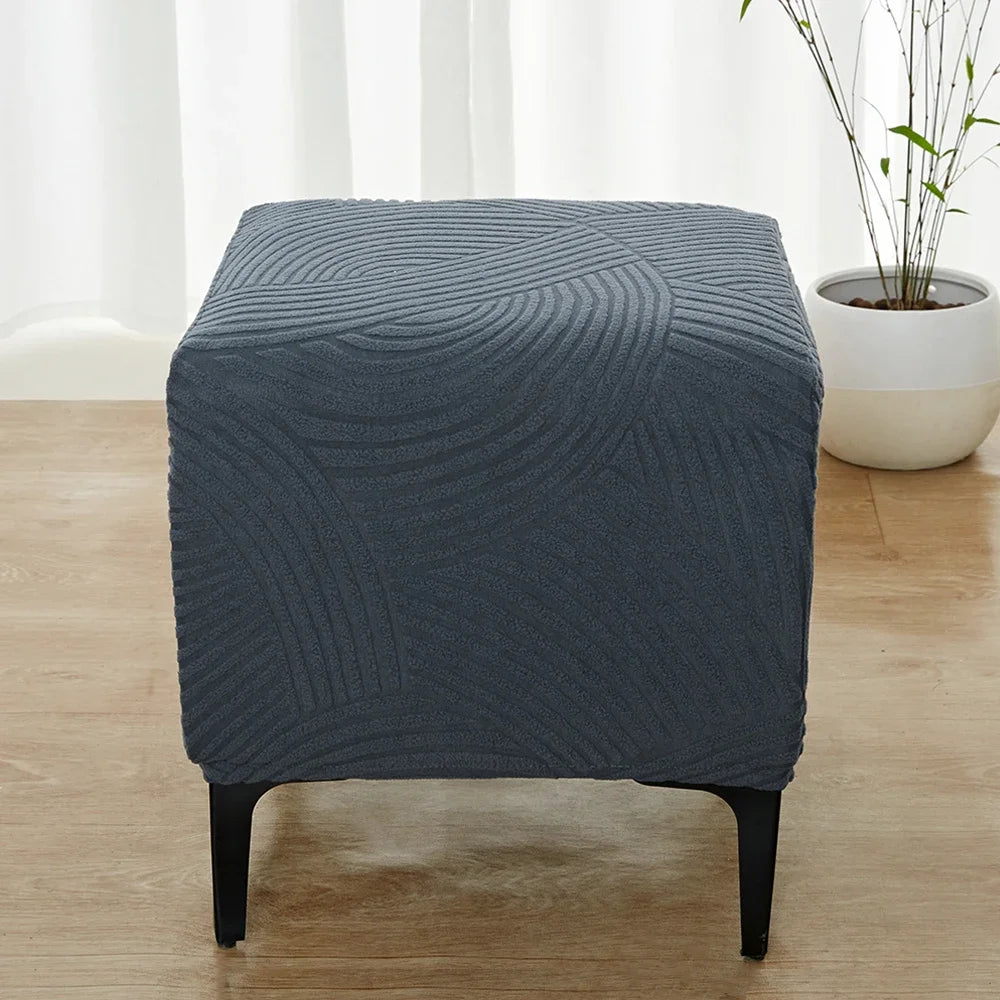A dark blue geometric jacquard stretch ottoman cover placed on a wooden floor.