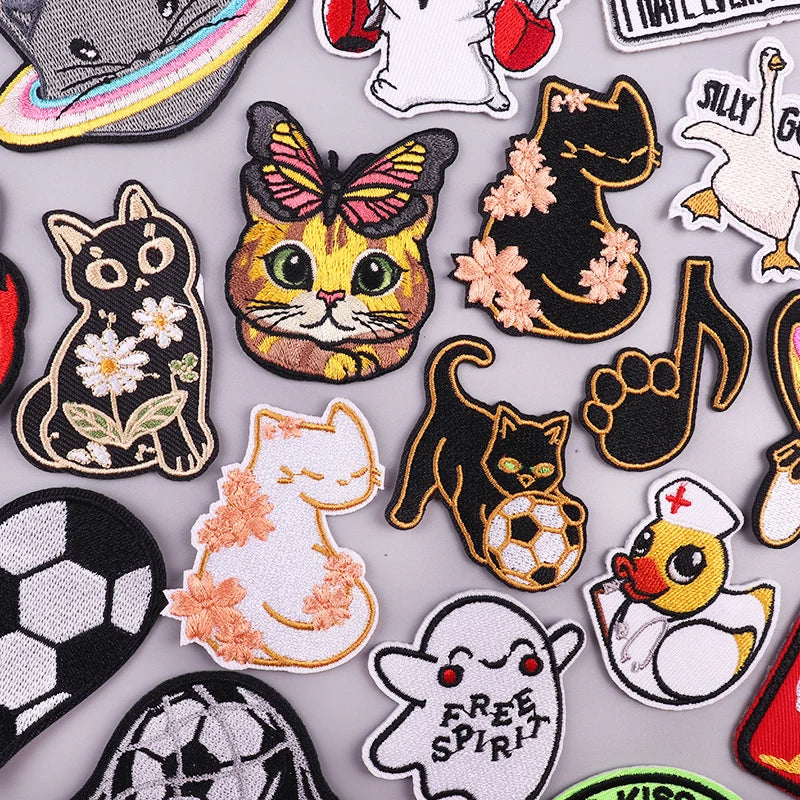 A collection of embroidered iron-on patches featuring various funny cartoon and animal designs like cats, a bat, and a duck.