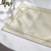 A square linen placemat with delicate white embroidery is displayed on a white surface.