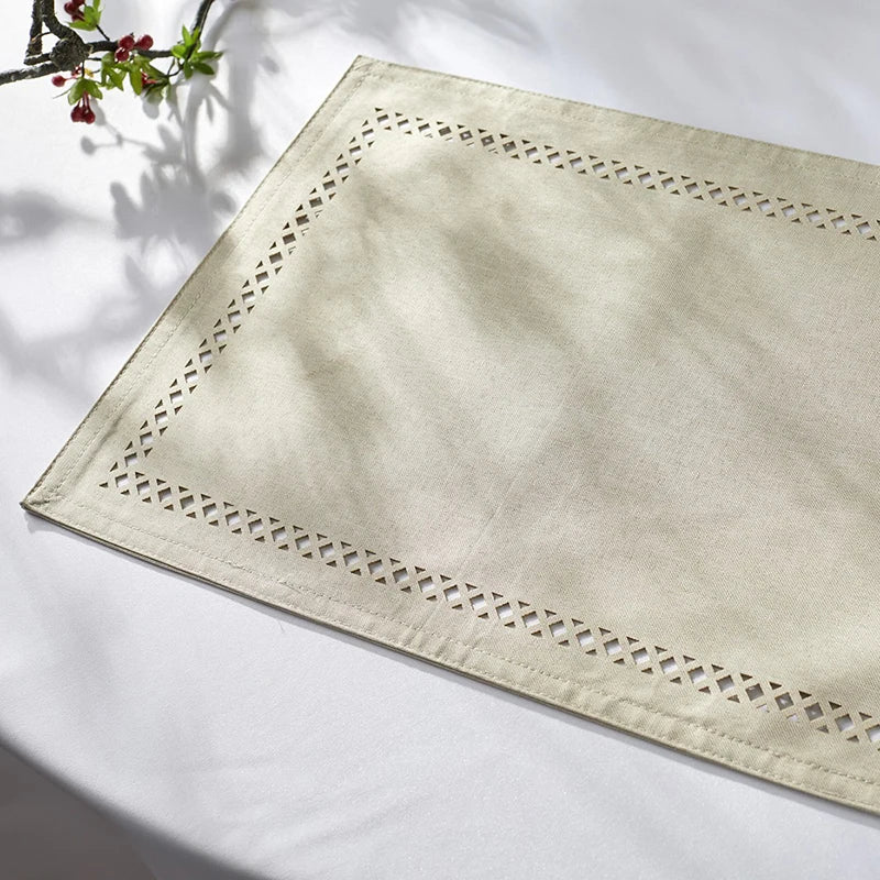 A square linen placemat with delicate white embroidery is displayed on a white surface.