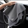 A gray ultra-soft coral fleece car drying towel is being held by a hand inside a car interior.
