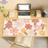 A pink floral mouse pad with orange and green accents is placed on a wooden desk next to a laptop.