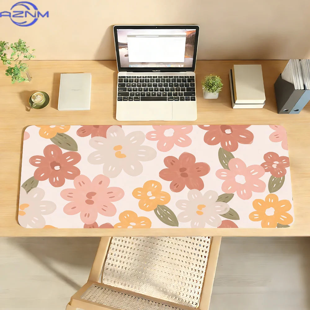 A pink floral mouse pad with orange and green accents is placed on a wooden desk next to a laptop.