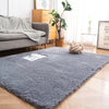 A gray Nordic furry accent rug placed on a light wood floor in a bright living room setting.
