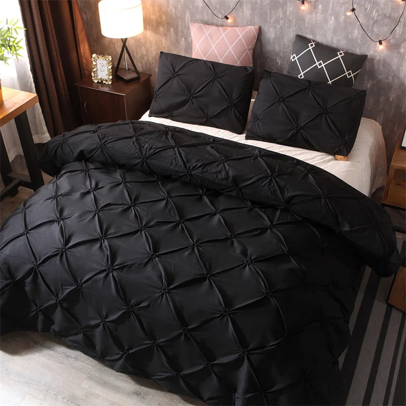 Black quilted comforter and pillow set displayed on a bed with pink accent pillows.