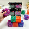 Une main tient un cube anti-stress violet et rose à côté de plusieurs cubes anti-stress verts, roses et oranges.