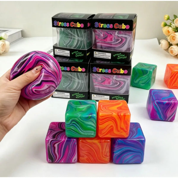 Une main tient un cube anti-stress violet et rose à côté de plusieurs cubes anti-stress verts, orange et violets.