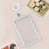 Sujetador de tarjetas de acrílico transparente con borde decorativo y anillo para llaves, apoyado sobre una superficie clara.