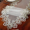 White embroidered mesh lace table runner with gold accents displayed on a dark wooden table.
