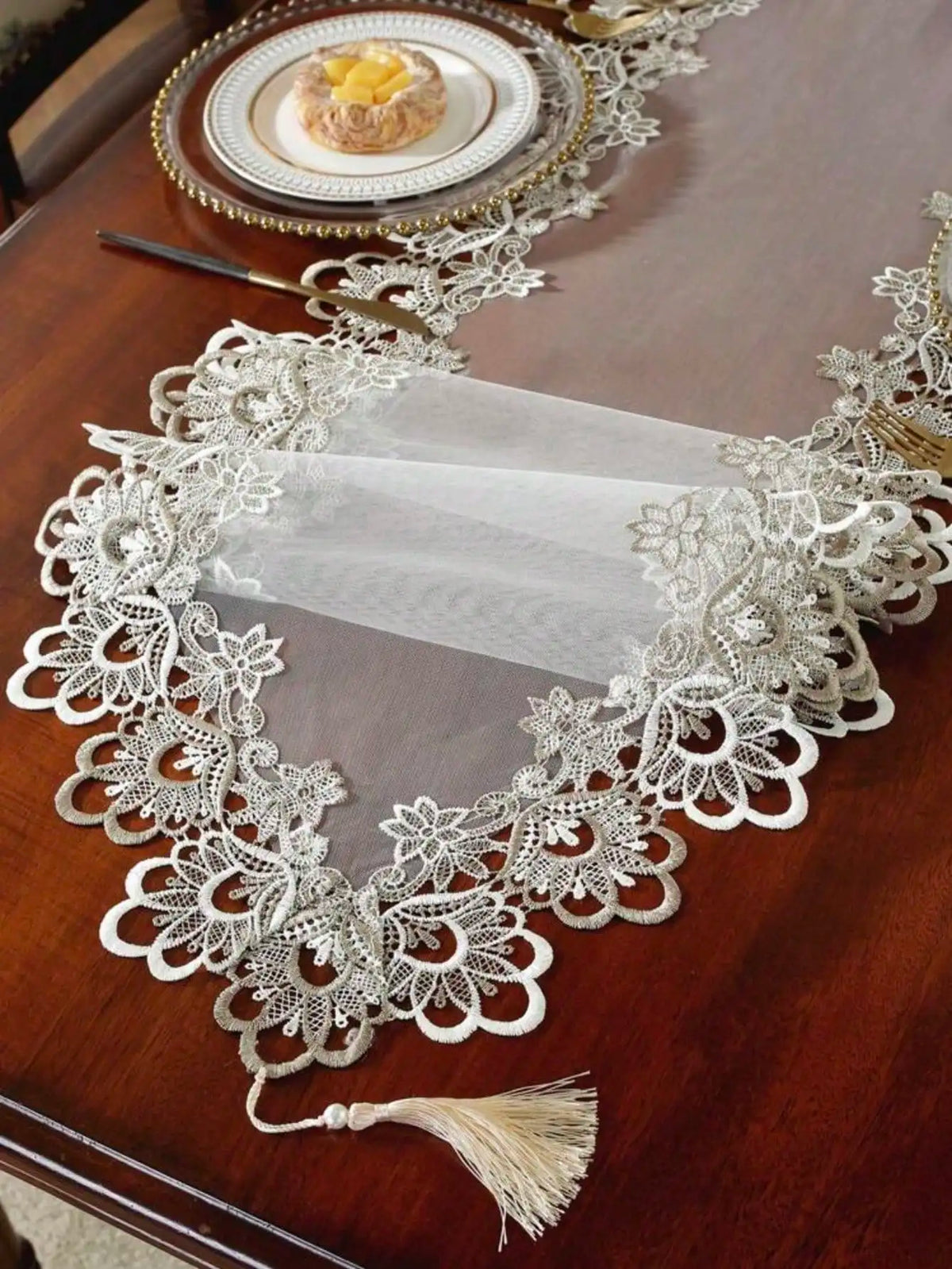 White embroidered mesh lace table runner with gold accents displayed on a dark wooden table.
