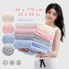 A woman holds a stack of pink and blue cloud velvet bath towels with a white top.