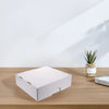A white foldable trading card storage box resting on a wooden table next to a small potted succulent.