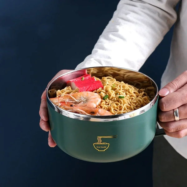A hand holds a green stainless steel ramen bowl filled with noodles, shrimp, and vegetables.