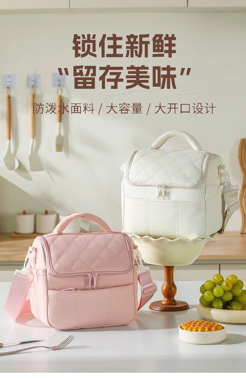 A pink insulated leakproof nylon lunch bag is displayed on a white table, with various utensils and a green fruit bowl nearby