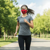A woman wearing a red reusable cycling face mask and clear goggles is running outdoors on a paved path.