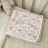 A floral muslin baby blanket with a light pink and cream pattern is shown resting on a white surface.