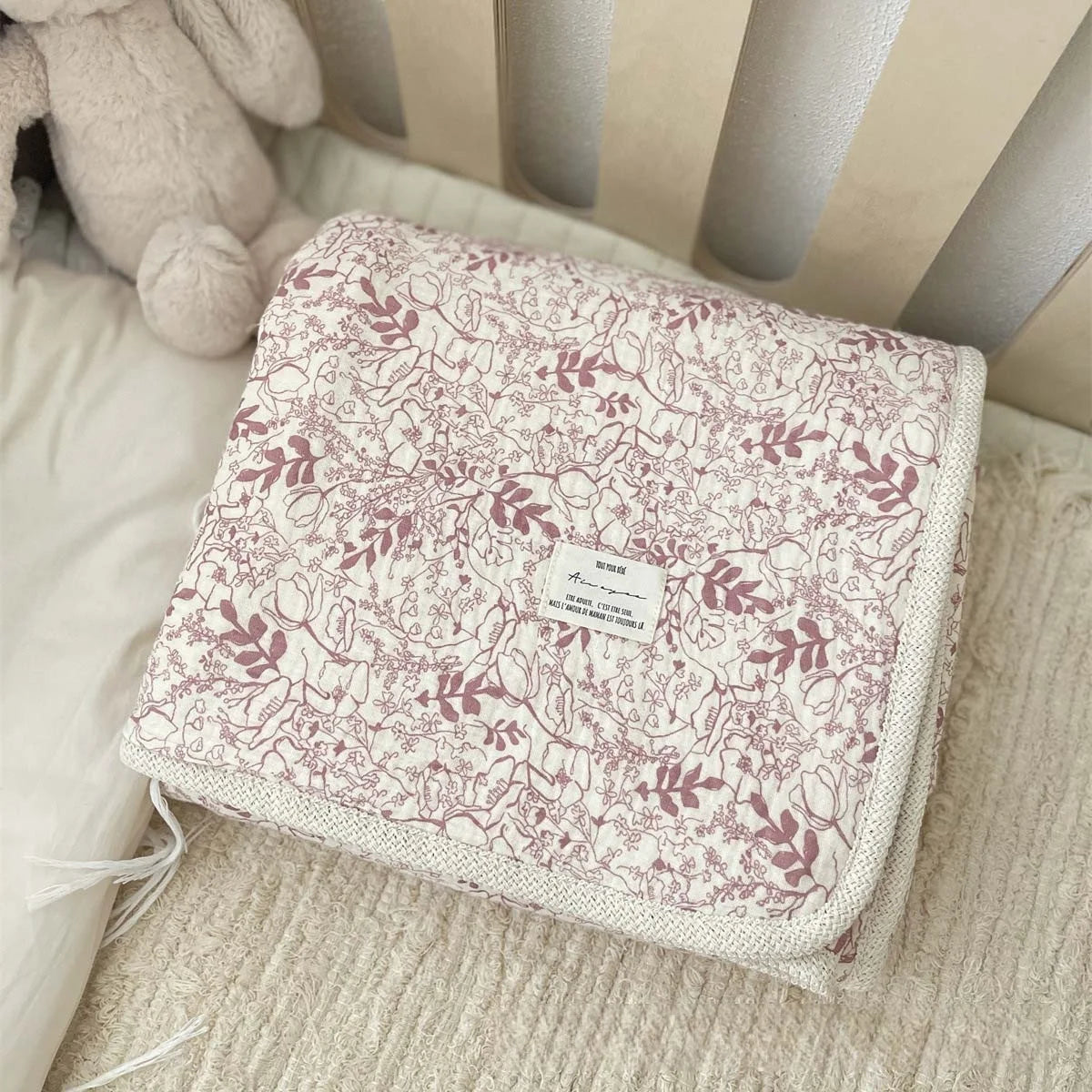 A floral muslin baby blanket with a light pink and cream pattern is shown resting on a white surface.