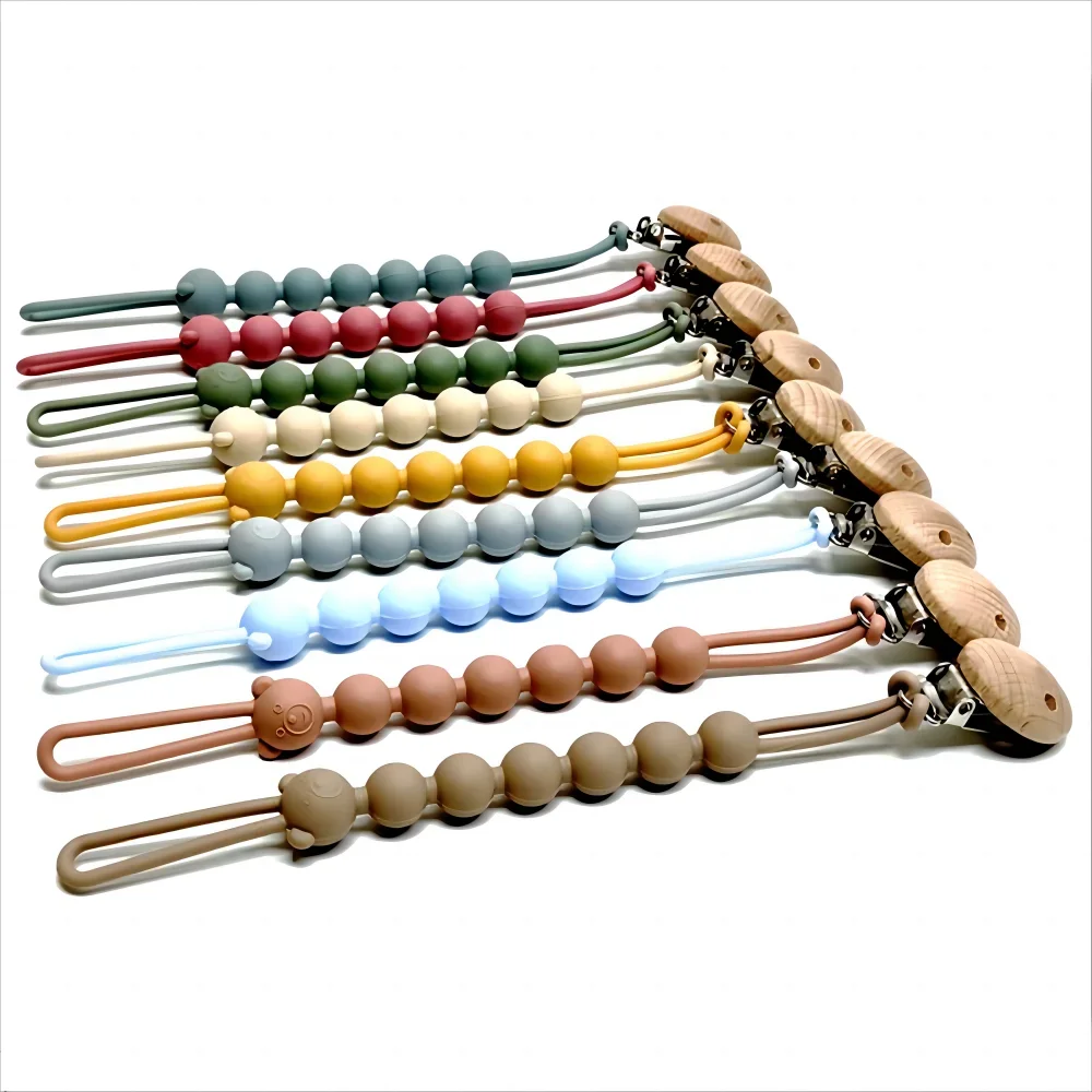 A display of food-grade silicone pacifier clips with anti-lost chains in various colors and wood accents.