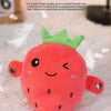A bright red strawberry shaped plush toy with green leaves and a smiling face resting on a white fluffy surface.